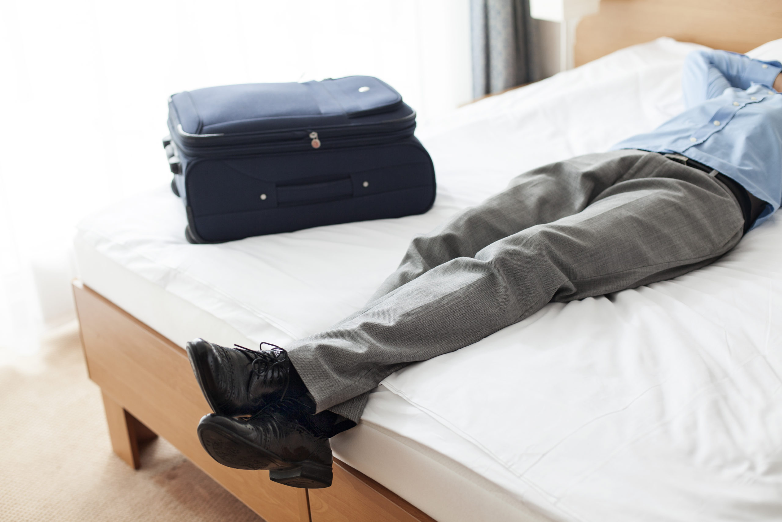 man laying in hotel bed with luggage